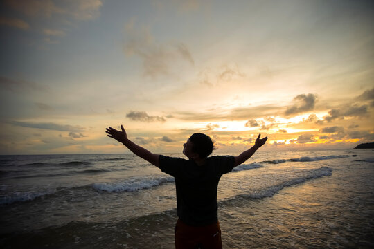 Silhouette of happy  man hand raising and watching sunrise over sea. Nature and beauty concept.