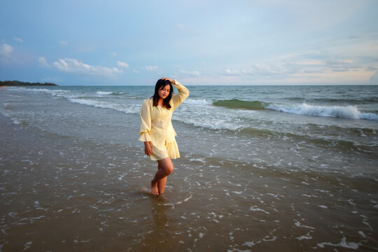 Beautiful Asian woman is happily strolling along the beach as the waves crash against her back. Happy girl rejoices in summer vacation.