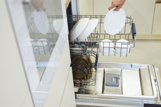Woman loading plates into an open dishwasher in a modern kitchen, carrying out daily domestic tasks