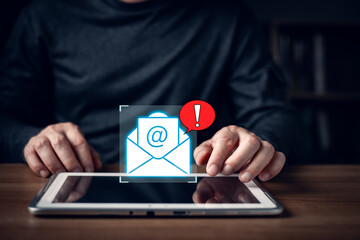 A person uses a tablet with a glowing email icon and red alert symbol representing email scam,spam messages,phishing risks,cybersecurity threats,online fraud,and the importance of digital protection.
