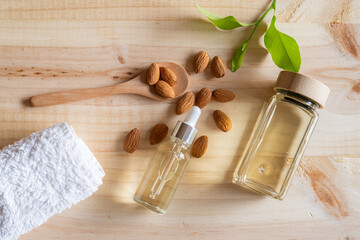 Almond oil in glass bottles with almonds, dropper and towel on wooden background, natural botanical...