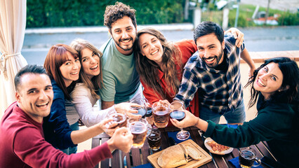 Happy diverse friends toasting with beer and wine at an outdoor party. Group of young people celebrating together, concept of friendship, community and weekend lifestyle.