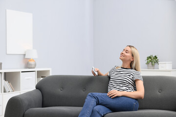 Obraz premium Woman with air conditioner remote control on sofa at home