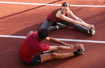 Couple in sportswear stretching before run at stadium, above view