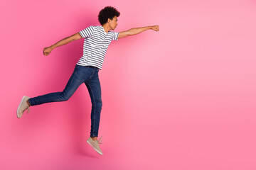 Young fashionable man leaping into action with determined pose on vibrant pink background...