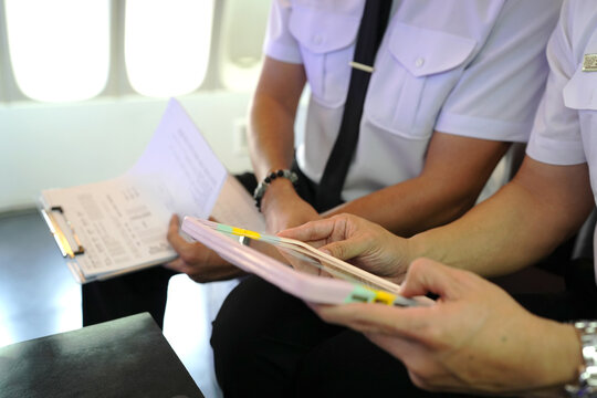 Male pilots preparing flight documentation, checking paper flight plan, log book and air traffic before take off and landing.