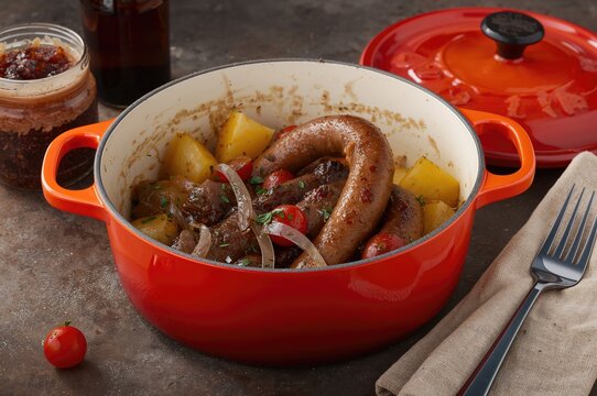 Sausage ring with potatoes and onions served alongside a jar of adjika in a bright orange pot