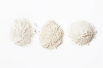 Three mounds of white powder including soda, flour, salt, and sugar displayed separately on a white surface.