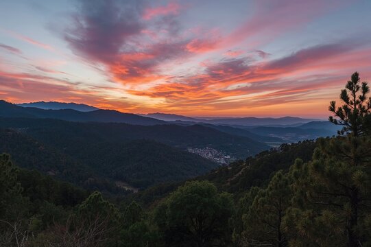 Colorful sunset over mountain ranges with lush green forests and pine trees in the foreground, horizontal landscape of a rural valley and hills