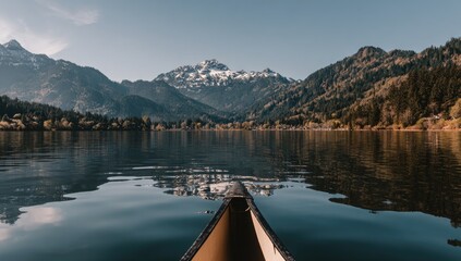Serene mountain lake vista from a canoe, showcasing calm water reflections and lush greenery.