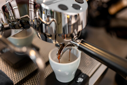 Close-up of espresso brewing from a professional machine into a ceramic cup on a digital scale, showcasing precision coffee preparation in a café or barista setting.