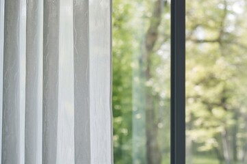 Sheer curtain with white designs against a window showcasing a fresh green spring landscape.