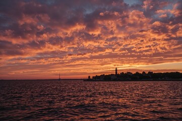 Sunset over the northern ocean with radiant pink and gold clouds, water reflections, and a beacon light. Majestic coastal scene with abstract textures and patterns.