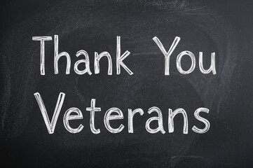 Gratitude to Veterans displayed on a chalkboard alongside a national flag on a rustic wooden surface. Celebrating national holidays honoring service members and labor.