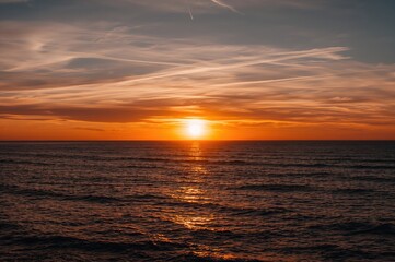 Obraz premium A serene sunset where the horizon blurs between water and sky, orange waves shimmering softly while a light breeze brushes your face. A stunning dusk ocean view illuminated by a magical light.