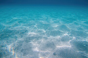 Obraz premium Underwater photo of a shallow seabed displaying multicolored light reflections on the sand due to light bending. abstract marine background