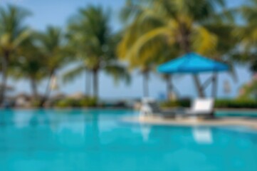 Out-of-focus swimming pool scene featuring a palm tree and a blue sunshade chair for a hotel resort summer gathering
