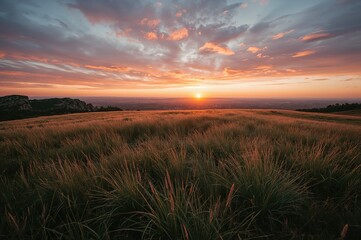 Obraz premium Sunset sky over a grassy meadow and rocky hill
