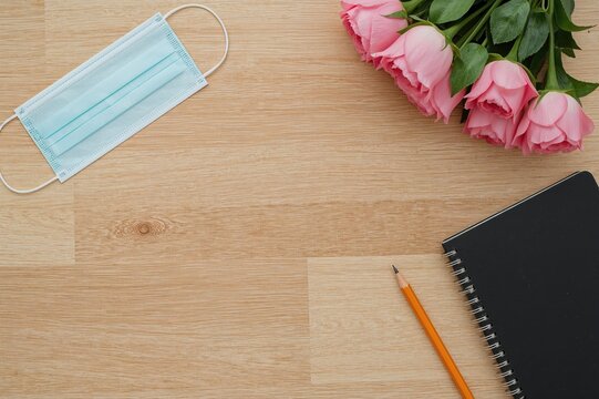 Educational theme separator featuring a blue protective face mask, dark journal, and a pink flower circle on wooden surface - Powered by Adobe