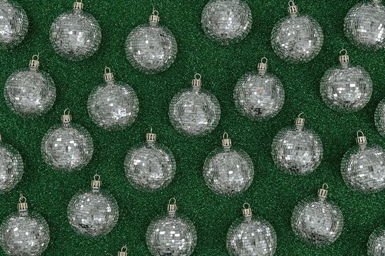 Glittering silver disco spheres on a verdant backdrop. Artistic festive design. 1990s vintage celebration theme. Holiday season setting. Overhead perspective. Flat arrangement. Empty area for text.
