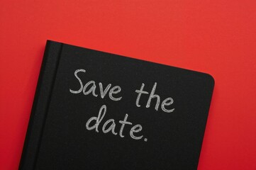 Red background with black notebook showing save the date message, conceptual symbol with copy space