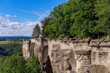 Old stone fortress wall with towers built on high sandstone cliffs surrounded by forest.