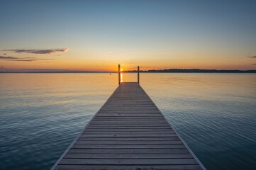 Sunrise over a tranquil lake with a wooden pier in the foreground