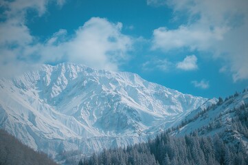 Fototapeta premium Breathtaking view of snowy peaks shining beneath a partly cloudy azure sky