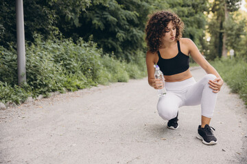Young sportswoman holding water bottle and feeling knee pain during running training