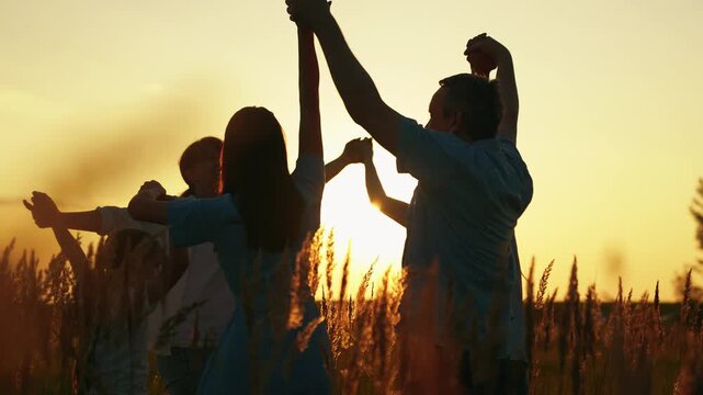 Family children happily dance in grass, enjoying nature at sunset. Happy mother father daughter dance in meadow at sunset, slow motion. Family party outdoors. Parents dad mom daughter dancing circle