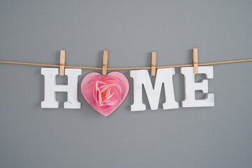 Letters spelling a cozy home dangle from a string with a heart and house design on a neutral backdrop. Celebrating love and comfort.