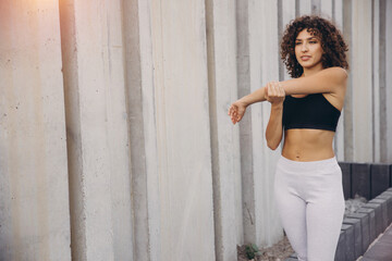 Young sportswoman stretching arm against concrete wall