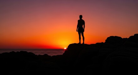 Obraz premium Silhouette of a person standing on a rock formation overlooking the ocean during a vibrant sunset view