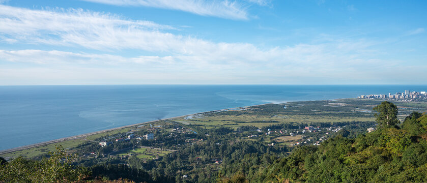 Panoramic view of ocean, coastal cityscape and green countryside from hilltop under clear blue sky