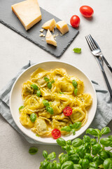 Tortellini pasta with parmesan, pesto and basil in a plate on a light  background with tomato, cheese and herb.