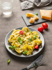 Tortellini pasta with parmesan, pesto and basil in a plate on a dark background with glass of water