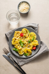 Tortellini pasta with parmesan, pesto and basil in a plate on a light background with glass of water