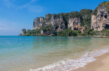 Cliffs, palm trees and sandy beach in Krabi, Thailand, with turquoise sea, limestone formations, and tropical vegetation under clear sky, showing coastal landscape travel destination in Andaman sea