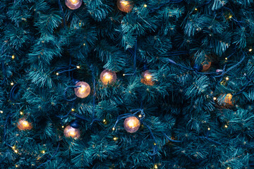 Warm glowing Christmas lights on green pine branches, festive background with golden bulbs and dark wiring, ideal for seasonal design or backdrop