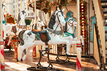 Decorative white horses on an old-fashioned merry-go-round at an outdoor fairground, captured in warm sunlight, evoking nostalgic childhood memories and festive vibes