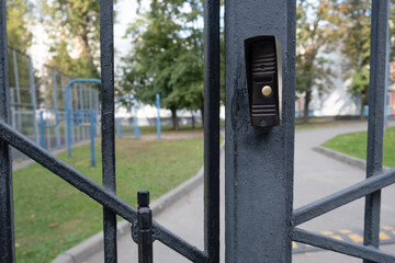 Close-up of a metal gate with intercom button restricting access to a fenced sports area in a typical city courtyard, symbolizing urban boundaries and security.