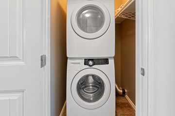 White dryer is stacked on top of another dryer in a small, dark room