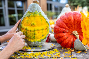 Hands of artist carve a large pumpkin into a comical face with exaggerated smile during Halloween...