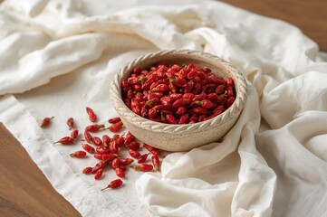 Braided rim bowl filled with goji berries sitting on a cloth-covered surface