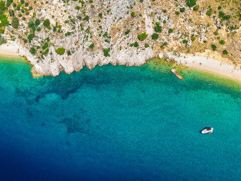 Hidden Croatian beach near Podgora protected by rocks with transparent lagoon textures and single boat anchored offshore