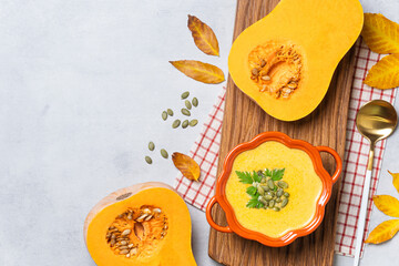 Pumpkin soup in bowl with fresh pumpkin and seeds.