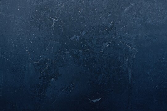 Extensive backdrop featuring a fractured blue wall and dark blue stone surface. Textured rock pattern with a muted tone. Broad banner layout. Shadowy grunge setting with ample copy space for creative