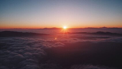 Obraz premium View from above showing a vivid sunset over distant peaks surrounded by soft, white clouds