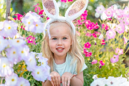 Positive little girl with bunny ears in the garden of flowers, Easter bunny