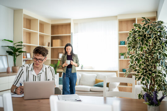 Young man working remotely at home with woman drinking coffee